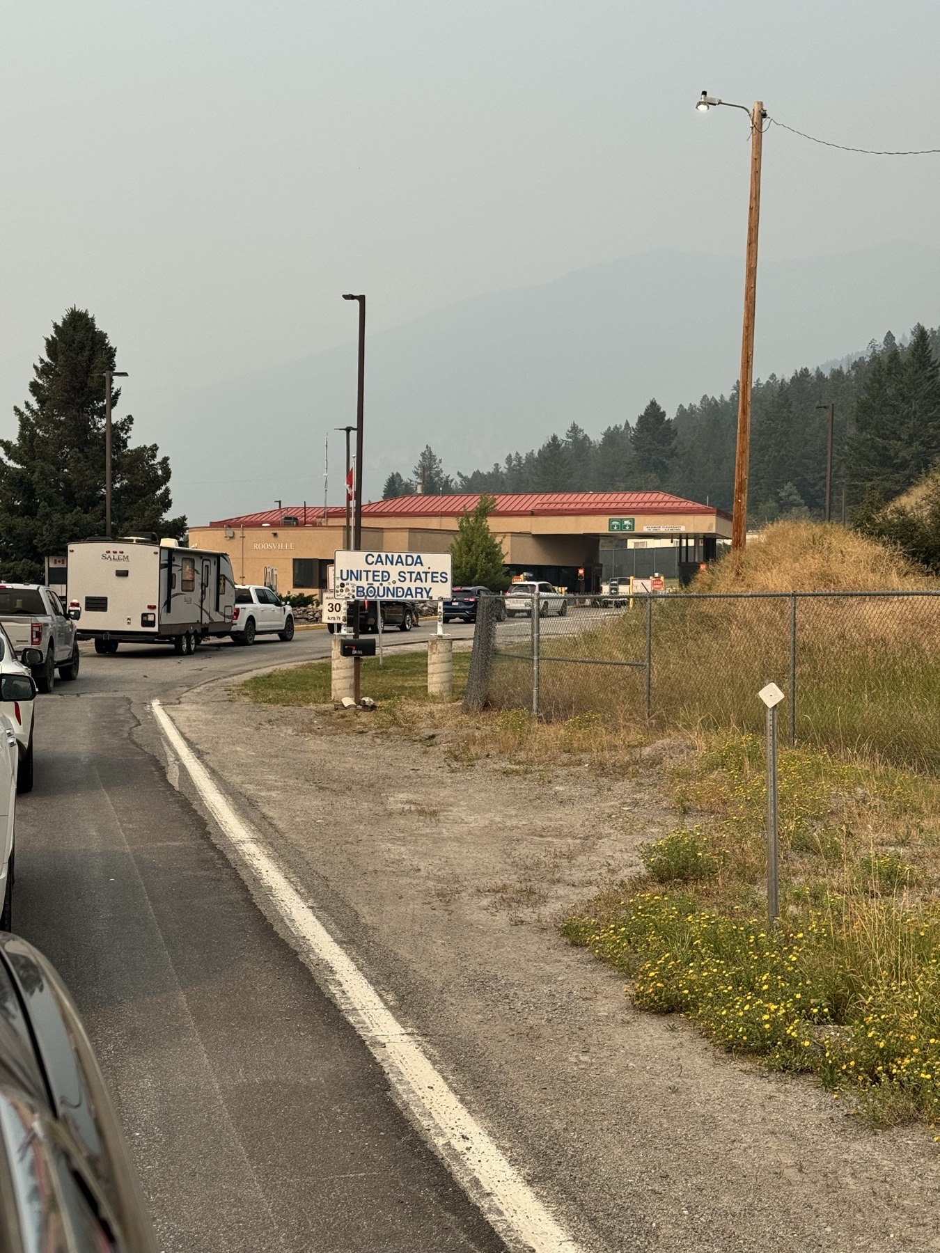 Road approaching the Canada–United States border through smoke-softened country